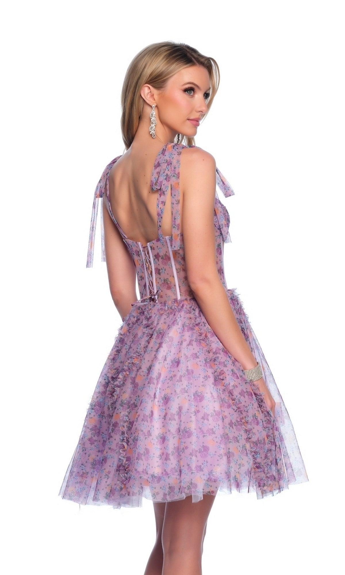 Woman in the Dave and Johnny Short Print Hoco Dress 11752, a sleeveless lavender floral party dress with a corset-style bodice and ribbon shoulder ties, glances over her shoulder against a plain white background.